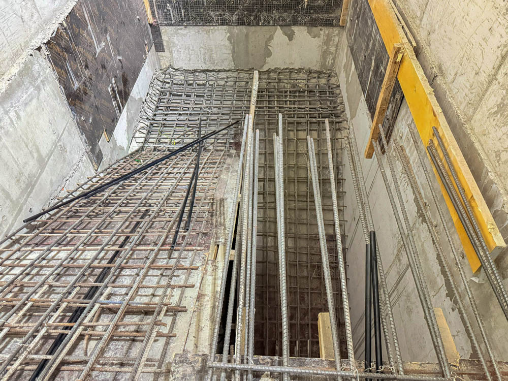 Beach Walk Iii By Imtiaz Construction site view showing a deep pit with exposed rebar and wooden supports, indicating ongoing building work.